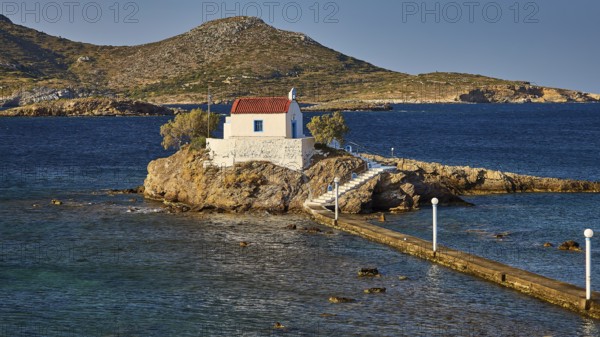 Whitewashed chapel on island, accessible via footbridge, surrounded by calm blue water, chapel, church, Agios Isidoros, rocky islet, Bay of Gourna, Kokkali, Leros, Dodecanese, Greek Islands, Greece