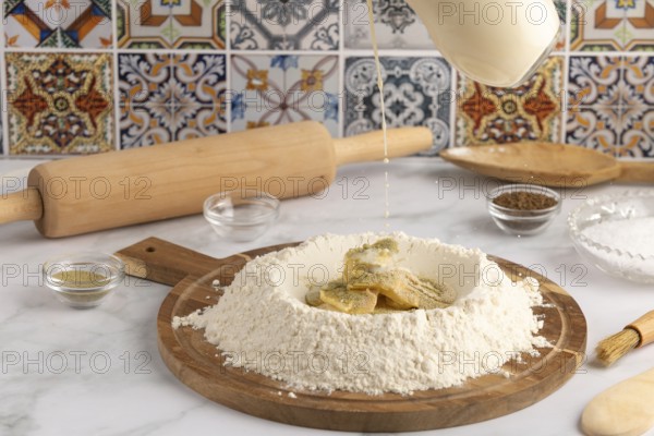 Milk is poured into a well of flour on a wooden board, surrounded by ingredients