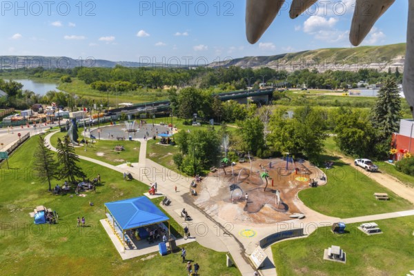 Drumheller city park offers a refreshing escape with splash parks, picnic areas, and a dinosaur statue overlooking the red deer river and surrounding badlands on a sunny summer day