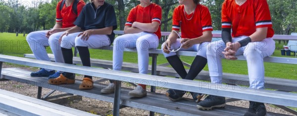 Young baseball players sitting together on bleachers, enjoying camaraderie and conversation after a challenging game, showcasing teamwork and sportsmanship