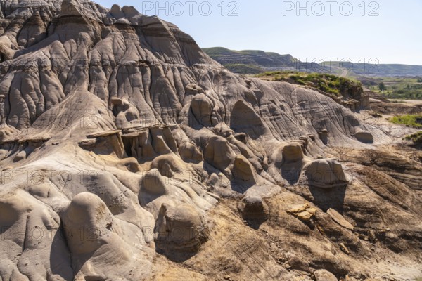 Sunlight illuminates the hoodoo badlands in drumheller, canada, showcasing unique rock formations and creating a dramatic landscape under a clear blue sky
