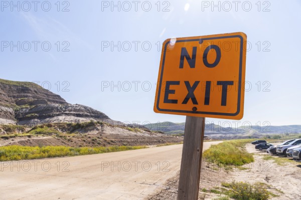 Bright orange no exit sign stands beside a dirt road leading into the arid badlands of drumheller, alberta, warning drivers of the dead end ahead