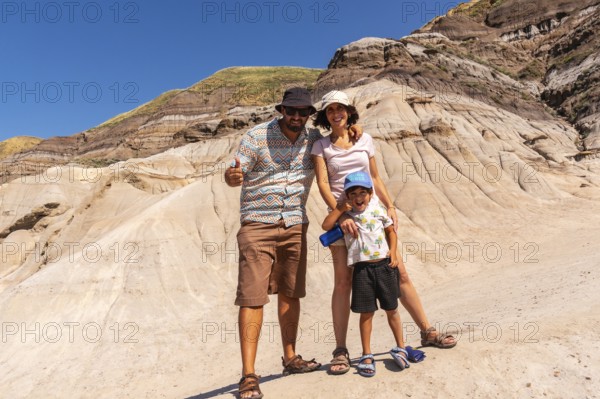 Happy family of tourists standing in front of the unique geological formations of drumheller, alberta, canada, giving thumbs up and enjoying summer holidays
