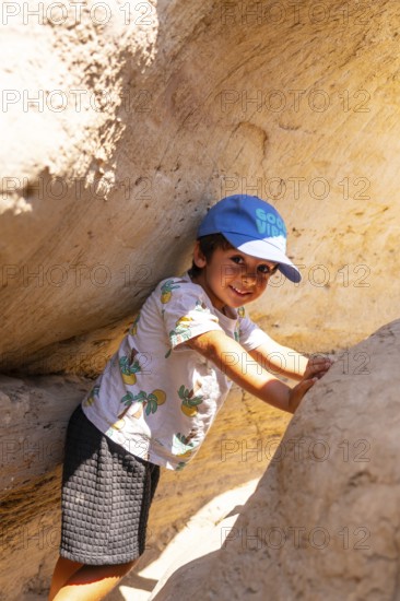 Young boy wearing a blue cap and a t shirt is exploring the unique sandstone hoodoo formations in drumheller, canada, touching the rock walls with a curious expression