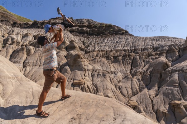 Father playfully lifting his son in the air at horseshoe canyon in drumheller, alberta, canada, enjoying a sunny day surrounded by unique geological formations
