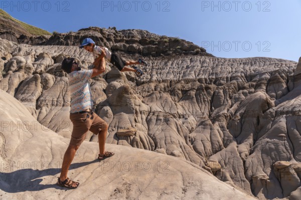 Tourist father lifting his son in the air, having fun in front of the unique geological formations of drumheller's hoodoos, in the canadian badlands of alberta, on a sunny day