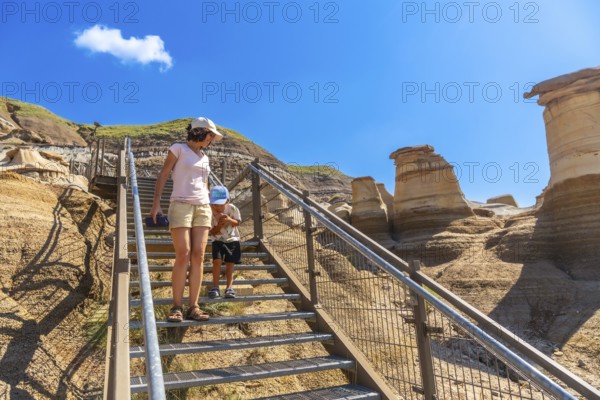 Mother and son descending metal stairs at the hoodoo trail in drumheller, alberta, canada, exploring unique geological formations on a sunny day