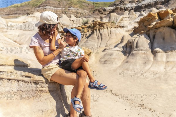 Mother holds her son on her lap, applying sunscreen to his nose during a sunny day exploring the unique hoodoo formations of drumheller, alberta