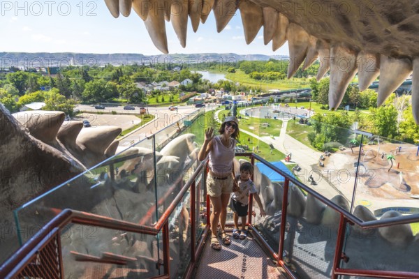 Tourists waving from the mouth of the world's largest dinosaur statue, taking in panoramic views of the red deer river valley and drumheller, alberta