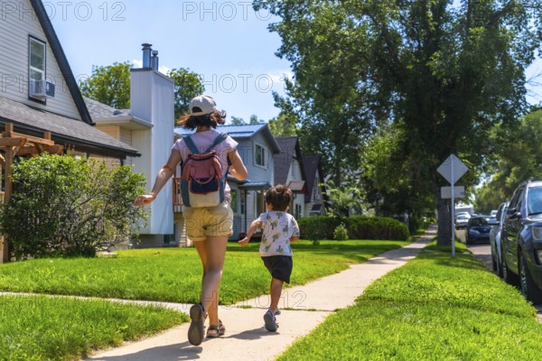 Mother and son running joyfully on the sidewalk in a residential neighborhood of drumheller, alberta, embracing the warmth of a sunny summer day filled with laughter and adventure