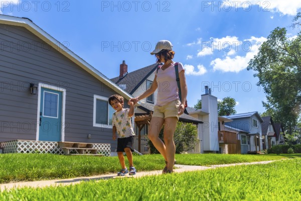 Happy mother and son holding hands and walking on a sidewalk in a residential neighborhood on a sunny summer day, enjoying quality time together