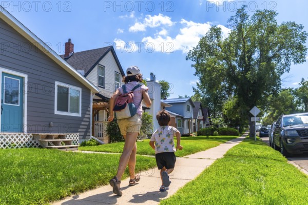 Mother with backpack and her son are running on the sidewalk in a residential neighborhood in drumheller, alberta, canada, during a sunny summer day