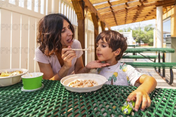 Mother feeds her son at a picnic table outside a restaurant in drumheller, alberta, canada, creating a heartwarming moment of family connection
