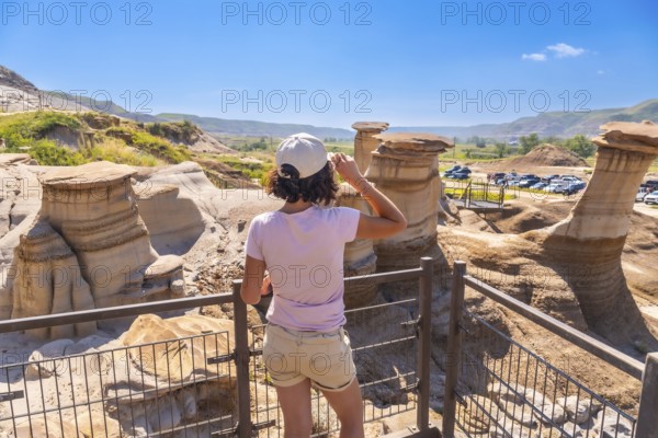 Young woman enjoying view of unique hoodoo rock formations at tourist attraction in drumheller, alberta, showcasing natural beauty and geological wonders of canadian badlands on sunny summer day
