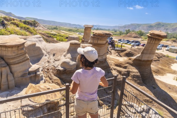 Tourist wearing a cap observing stunning hoodoo rock formations in drumheller valley, alberta, canada, a unique geological landscape attracting visitors worldwide