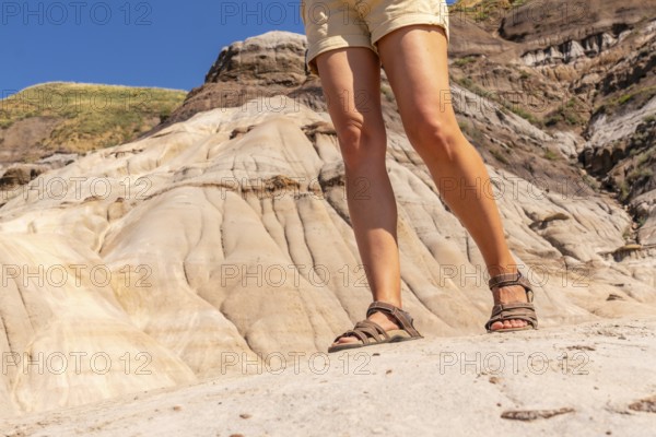 Female tourist wearing hiking sandals standing on the edge of a hoodoo in drumheller, alberta, canada, enjoying the unique geological formations and the sunny weather