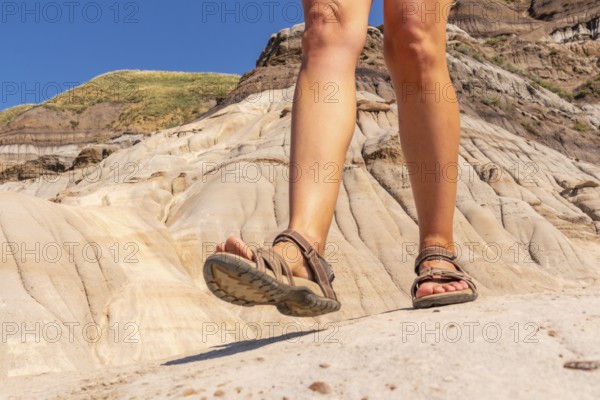 Female tourist wearing sandals walking on the rocky terrain of the hoodoos in drumheller, alberta, canada, exploring unique geological formations on a sunny day