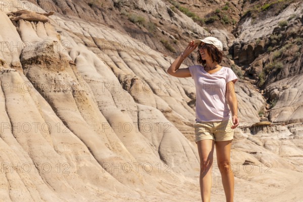 Female tourist shielding her eyes from the sun while exploring the unique hoodoo rock formations in drumheller, alberta, a popular destination for geology enthusiasts