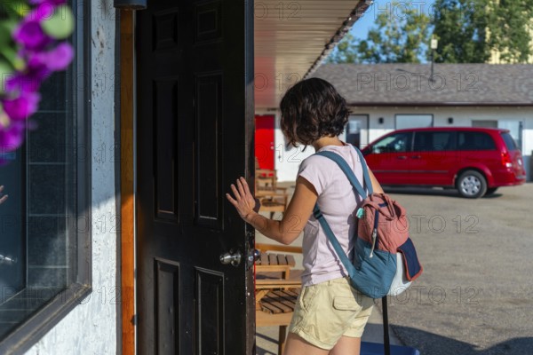 Female tourist with a backpack and rolling suitcase opening the door to a motel room after a long road trip, feeling excitement and relief while ready to relax and unwind