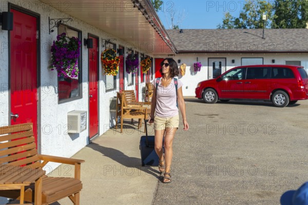 Female tourist pulling her luggage while strolling towards her room at a roadside motel, enjoying a sunny summer road trip vacation filled with adventure and exploration