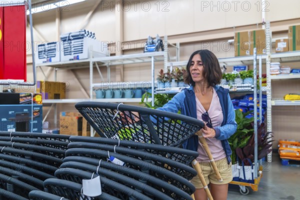 Smiling female customer selecting new outdoor furniture, picking up hanging egg chair in warehouse, shopping for home goods, enjoying weekend retail therapy