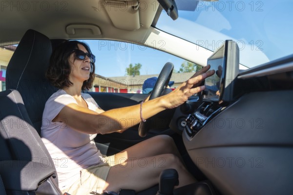Woman wearing sunglasses driving a modern car and using gps navigation system on the dashboard touchscreen while holding the steering wheel