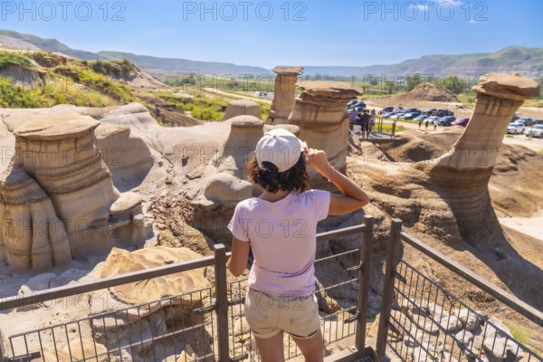 Young woman shielding her eyes from the sun while admiring unique hoodoo rock formations in drumheller valley, a stunning natural wonder in alberta, canada