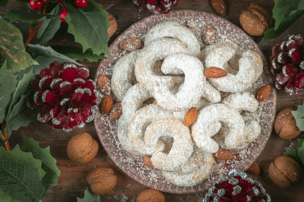 Vanilla croissants on a plate surrounded by walnuts, almonds and Christmas decorations