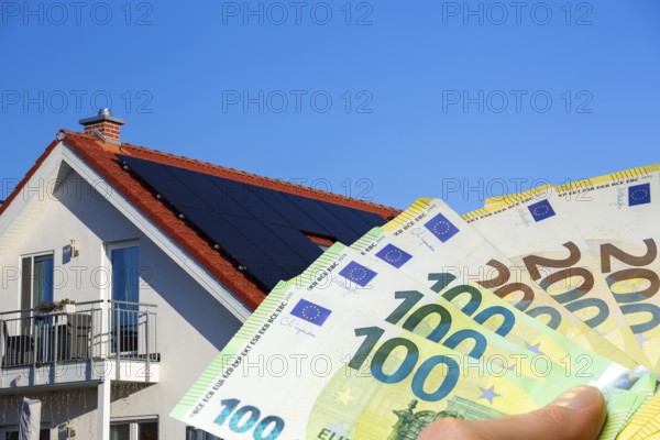 (Photo montage) Man holding euro banknotes in front of a solar roof