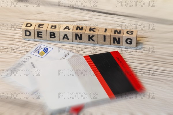 Debanking symbol: Letter cubes in front of a cut bank card show the word DEBANKING