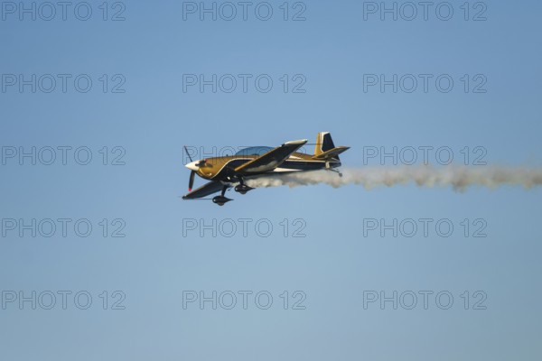 Golden stunt aerobatic plane performing stunts in blue sky with smoke trail. Concept of speed, difficulty, precision, risk