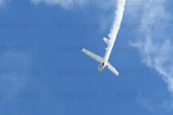 Stunt aerobatic plane performing stunts in blue sky with smoke trail. Concept of speed, difficulty, precision, risk, challenge