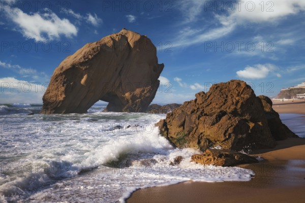Penedo do Guincho, a large boulder rock arch at Praia da Santa Cruz, Portugal, with ocean waves and sandy beach