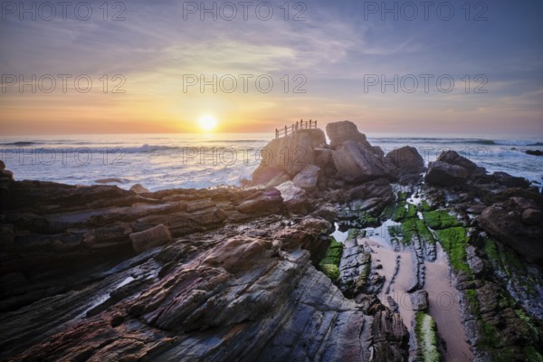 Scenic rock formation at Praia da Santa Cruz, Portugal, with ocean waves and vibrant sunset sky reflecting on the rocks
