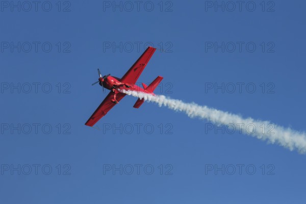 Red stunt aerobatic plane performing stunts in blue sky. Concept of speed, difficulty, precision, risk