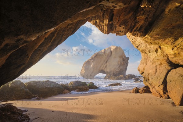At Praia da Santa Cruz, Penedo do Guincho stands majestically as waves crash into the sandy beach beneath a colorful sunset