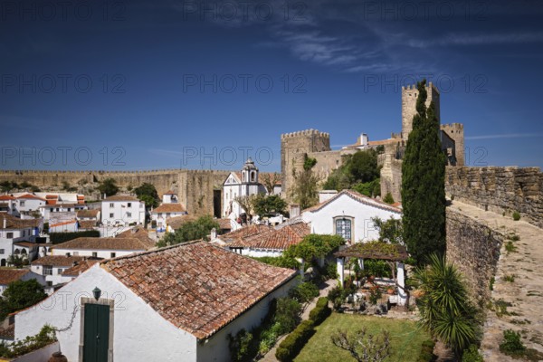 Stunning Obidos castle overlooking traditional Portuguese houses and rooftops under a clear blue sky. Portugal