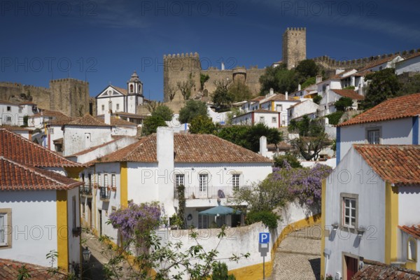 Obidos town featuring white houses, vibrant rooftops, and the impressive medieval castle under a blue sky. Portugal