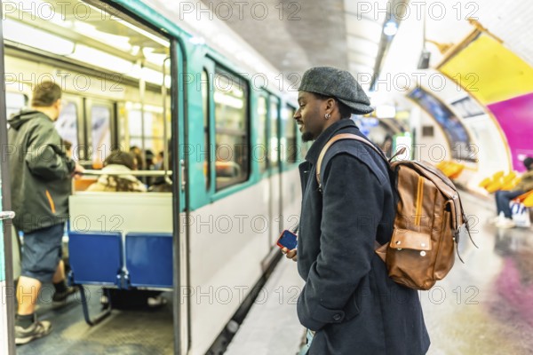 Young man stands on a bustling paris metro platform, looking toward an open train door as passengers board and depart during a busy daily commute