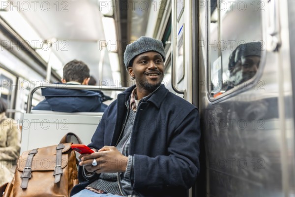Young black man traveling on public transport, smiling and holding a smartphone, showcasing urban lifestyle and daily commute connected with technology
