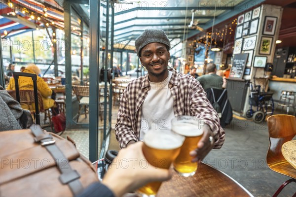 Young man smiling and clinking beer glasses with a friend in a casual pub, celebrating friendship, laughter and relaxed weekend vibes in an urban hangout