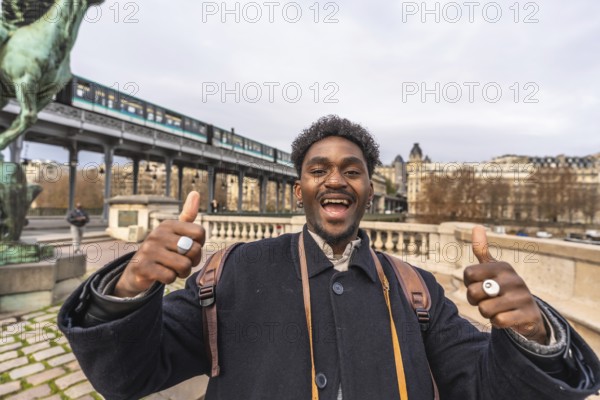 Enthusiastic young black man expressing happiness and positivity with a thumbs up gesture, traveling and exploring the city of paris with an elevated train in the background