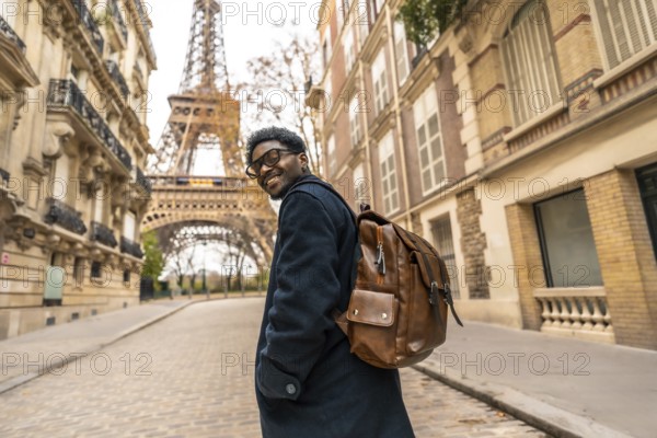 Young man smiling and turning back while exploring a historic street in paris, enjoying his leisure travel with the iconic eiffel tower visible in the background