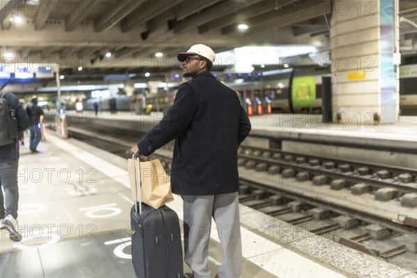 Man standing on a train station platform with his luggage, waiting for his train, embodying travel, journey, and the efficiency of public transportation