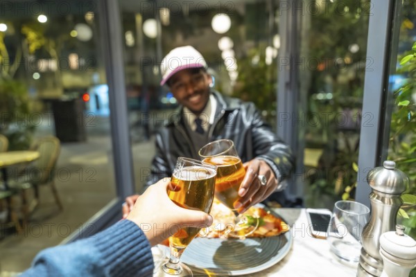 Diverse friends celebrating a successful night out, clinking beer glasses in a cheers gesture, sharing food at a modern restaurant table with city lights in the background