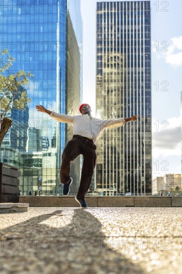 Young black man jumps with arms wide, celebrating joy and freedom against modern skyscrapers and blue sky in a sunny urban business district, energetic and optimistic