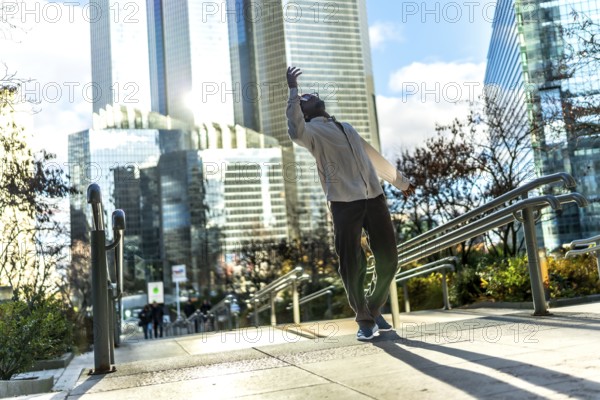 Man finding personal freedom and expressing himself through expressive urban dancing on a public stairway in a modern city against a bright sky and contemporary architecture during daylight