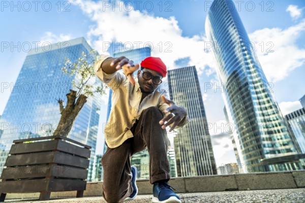 Young black man performing a dynamic street dance pose, capturing urban culture and a cool lifestyle against a modern city skyline with skyscrapers and a bright blue sky