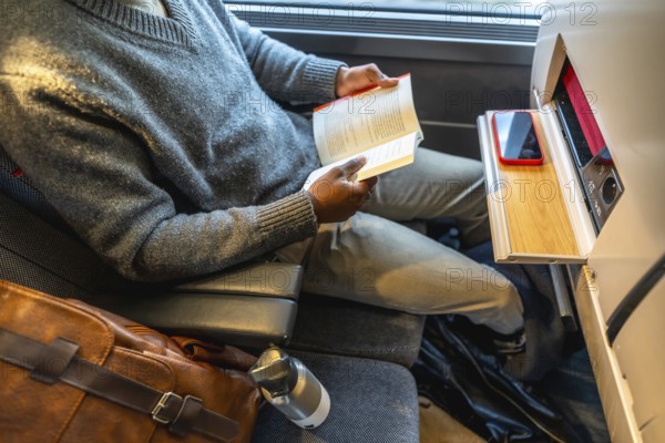Black man enjoying a book while traveling by train, reflecting concepts of leisure, modern transportation, and connected commutes for work or personal journeys