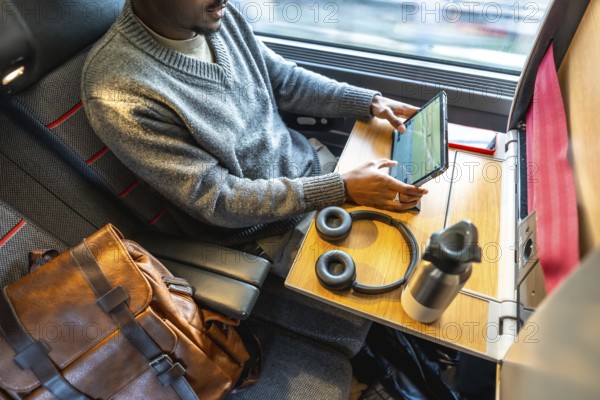 Man finding comfort and productivity while traveling for business, utilizing his tablet and staying connected during a train journey with a window view